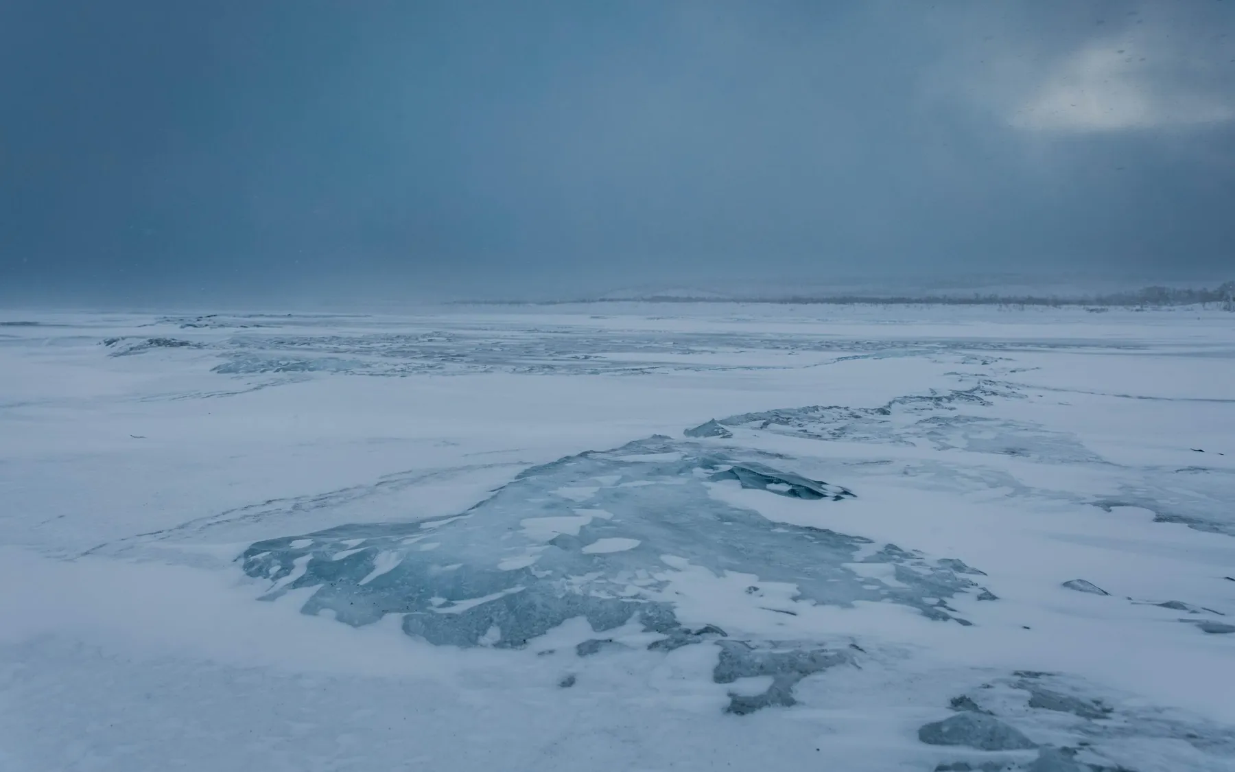 Wind-swept frozen lake: bluish ice showing through the snow, under a stormy sky