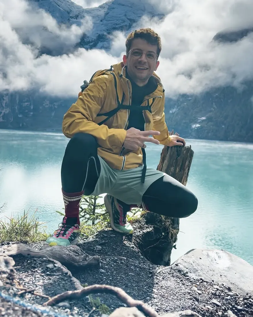 Hugo Paradis accroupi au bord d’un lac de montagne turquoise, veste jaune