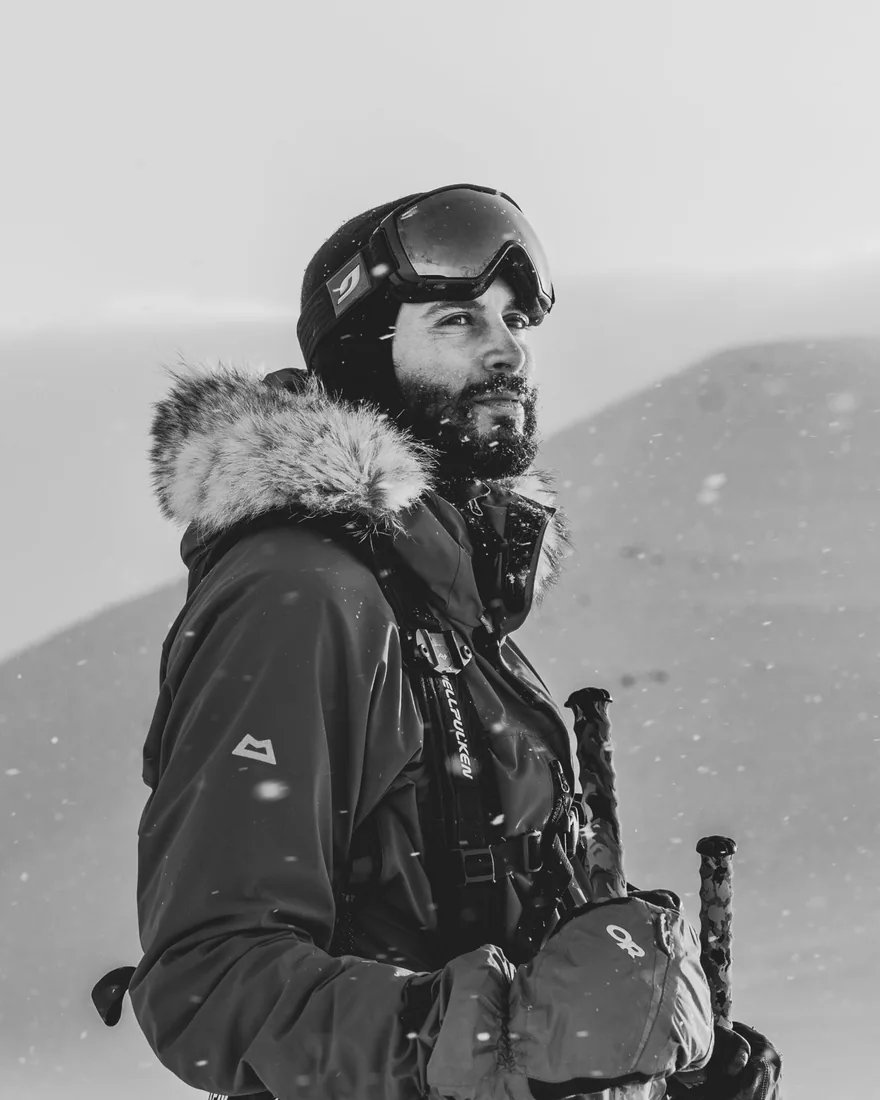 Portrait en noir et blanc de Moufid Taleb sous la neige, capuche fourrée et masque de ski relevé